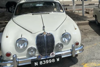 Front view of a white vintage Jaguar Mark 2 luxury sedan with chrome grilles and classic round headlights parked on a street.